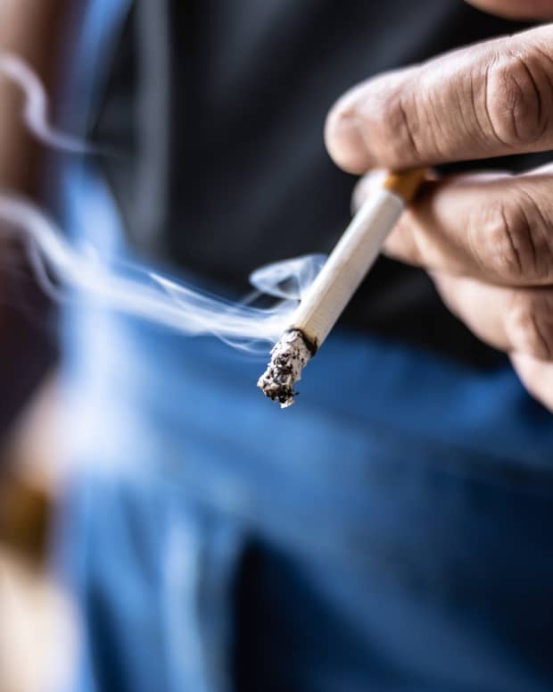 Man holding a smoking cigarette in his hand.