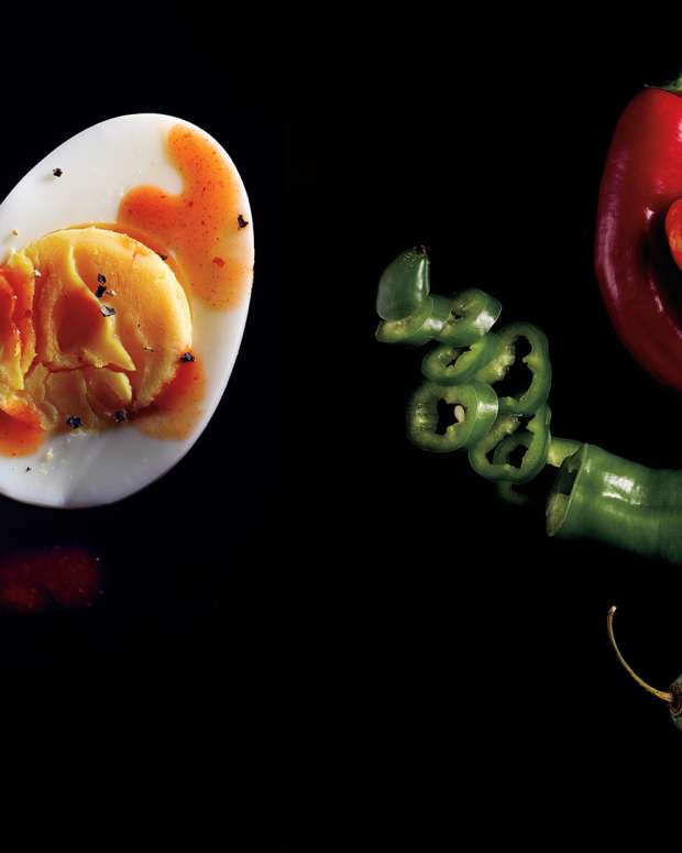 Black background with hard-boiled egg topped with hot sauce and variety of peppers