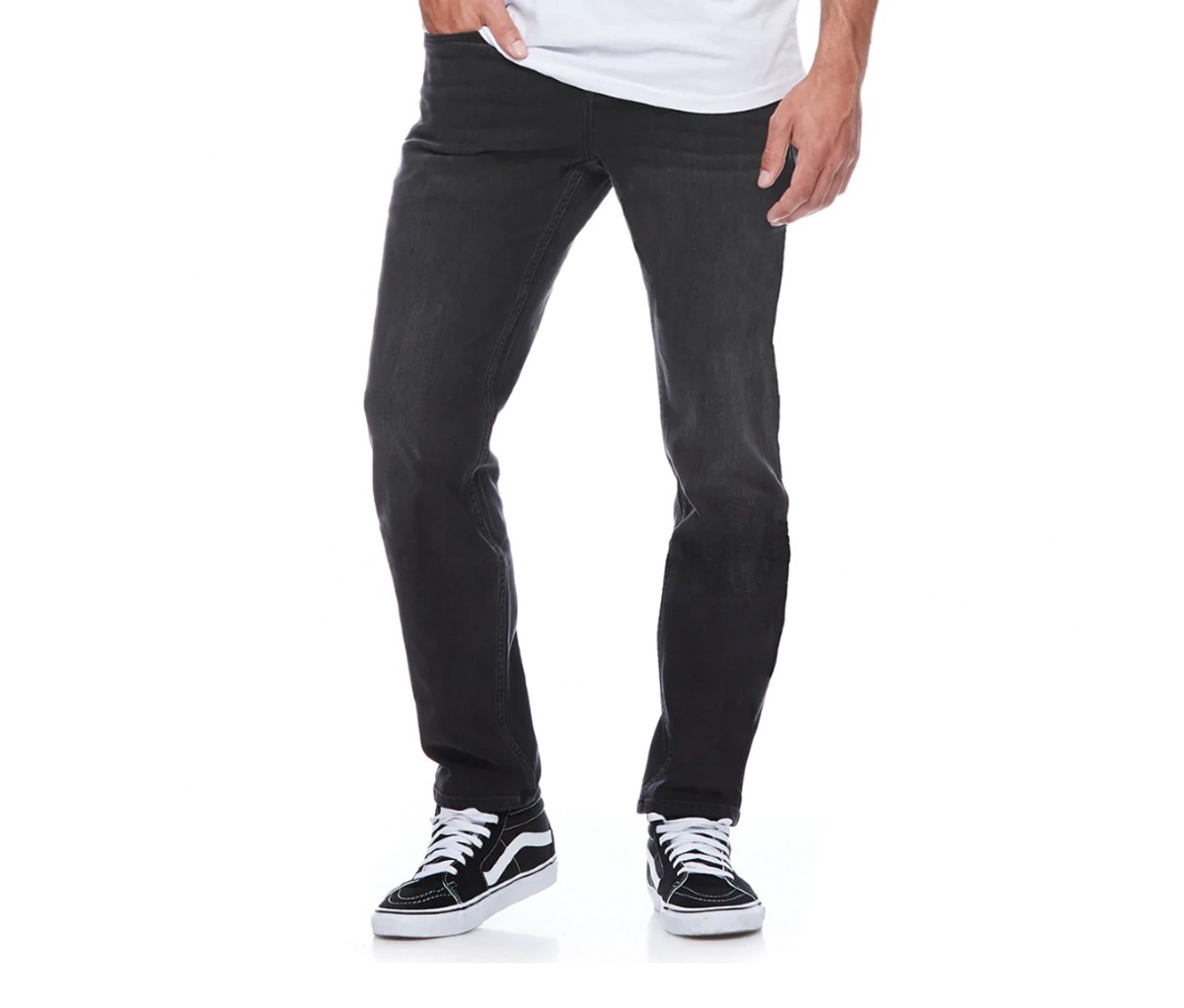 Man in white T-shirt wearing dark blue jeans and skate sneakers on a white background.