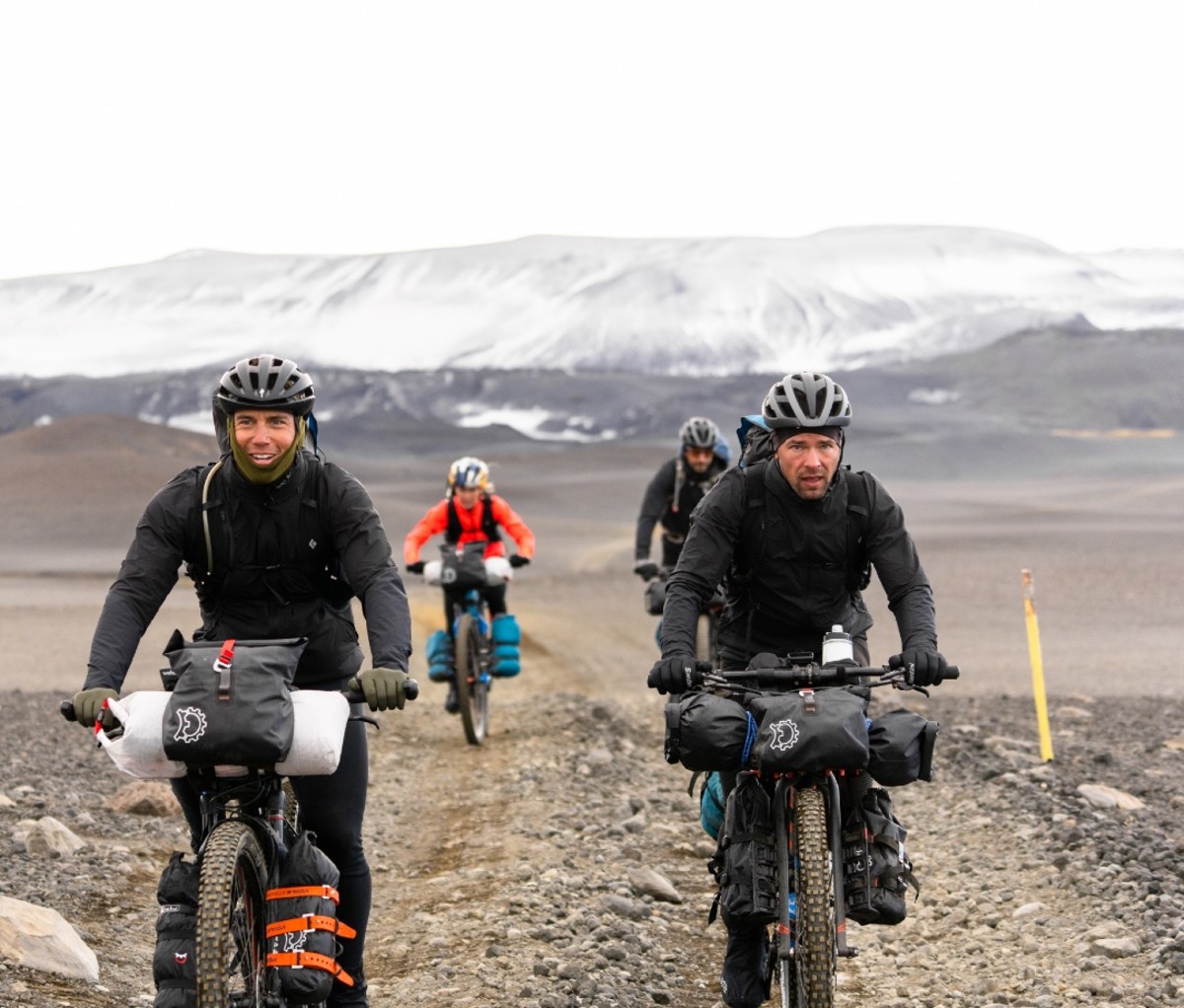 Chris Burkard, Emily Batty, Adam Morka, and Eric Batty biking with glaciers in the background.