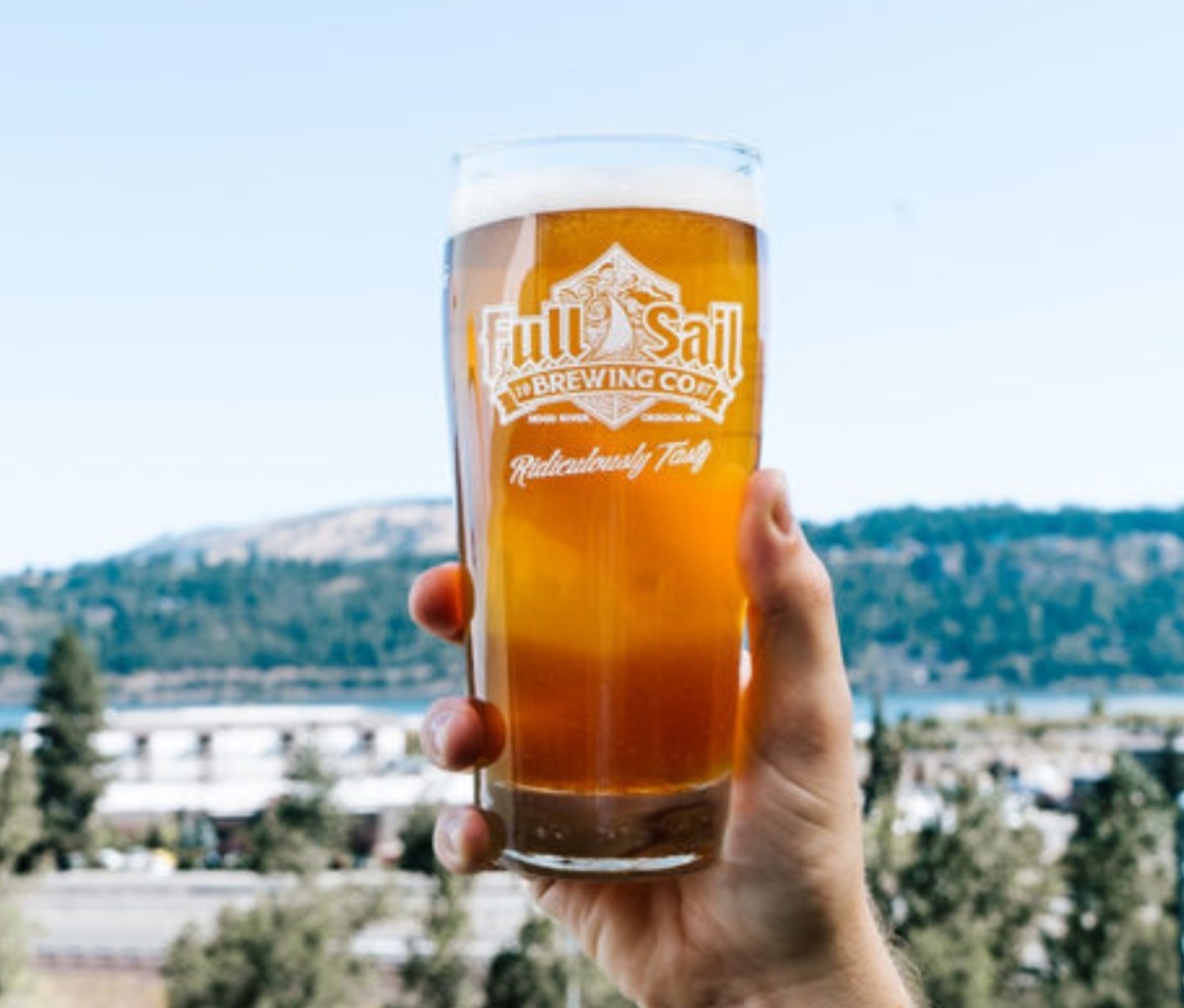 Man's hand holding glass of beer in Full Sail Brewing Co. glass