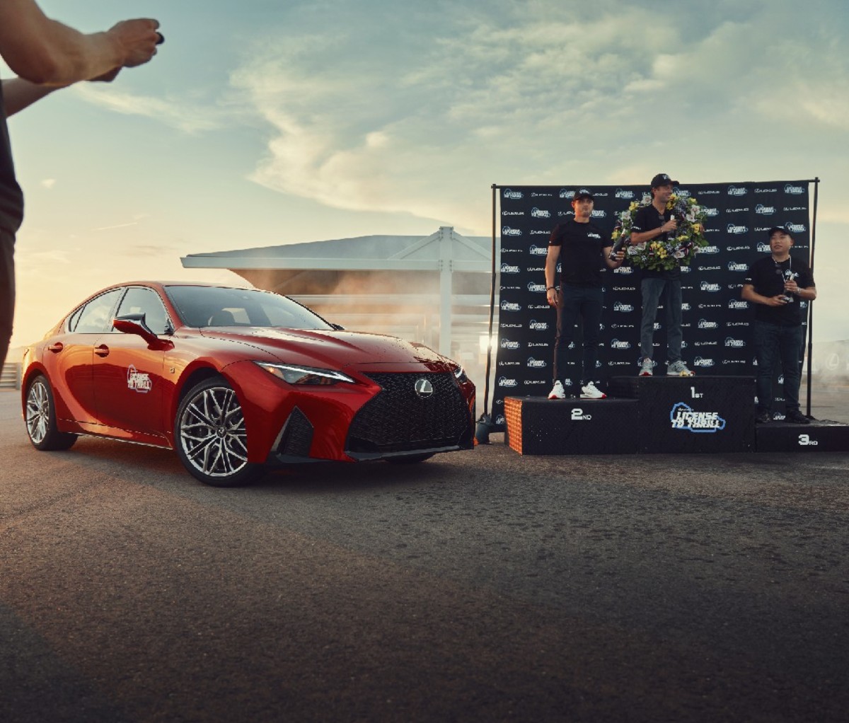 Red sports car to the left of three racers standing on podium