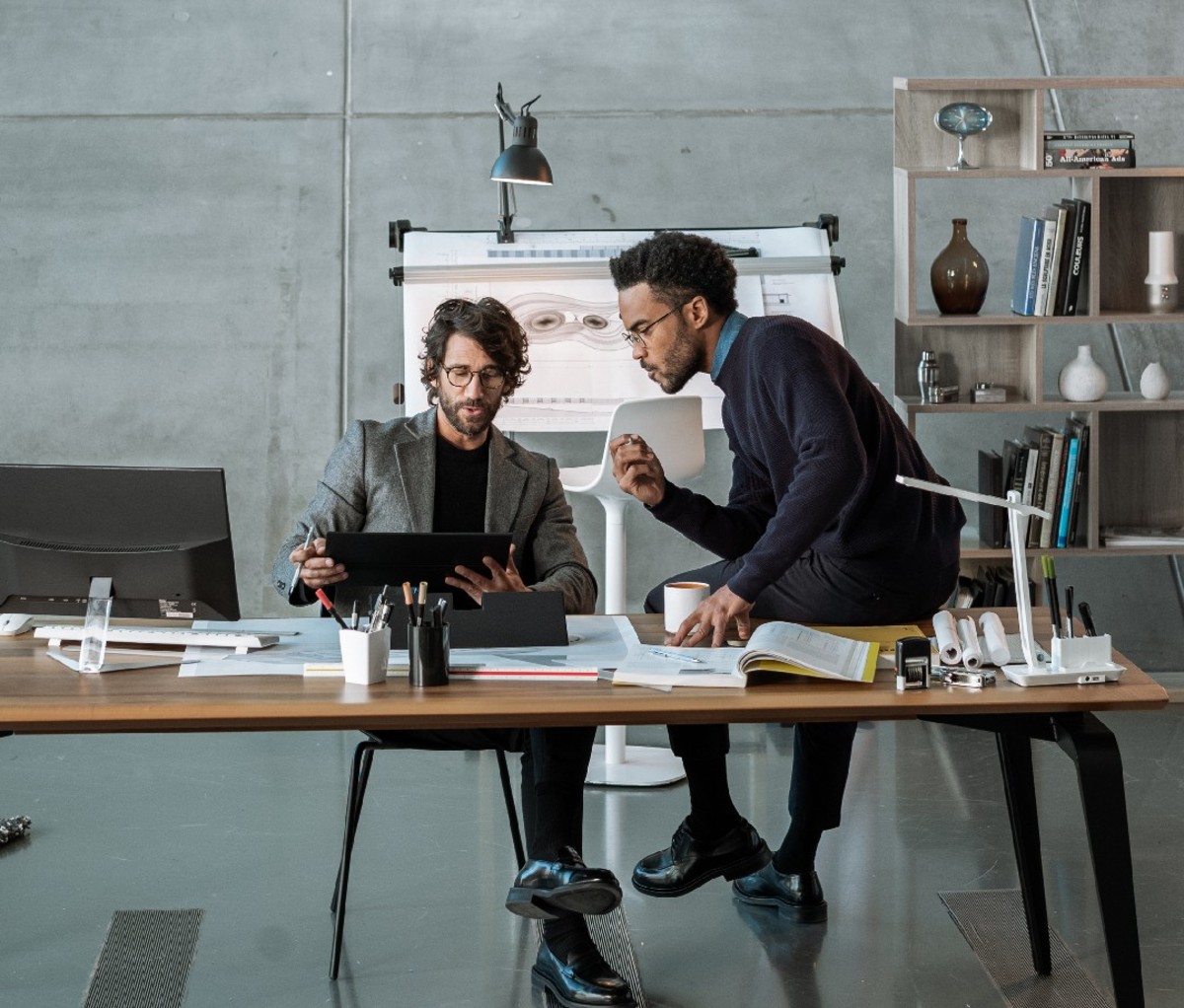 Two men sitting at desk wearing prescription eyeglasses looking at computer together