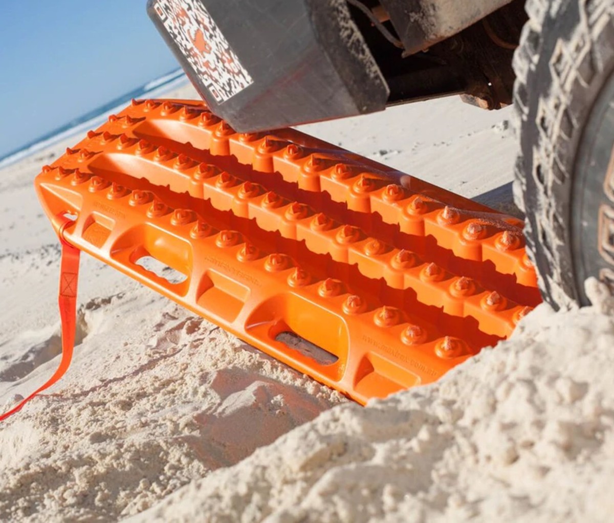 Orange recovery board under wheel of truck in sand