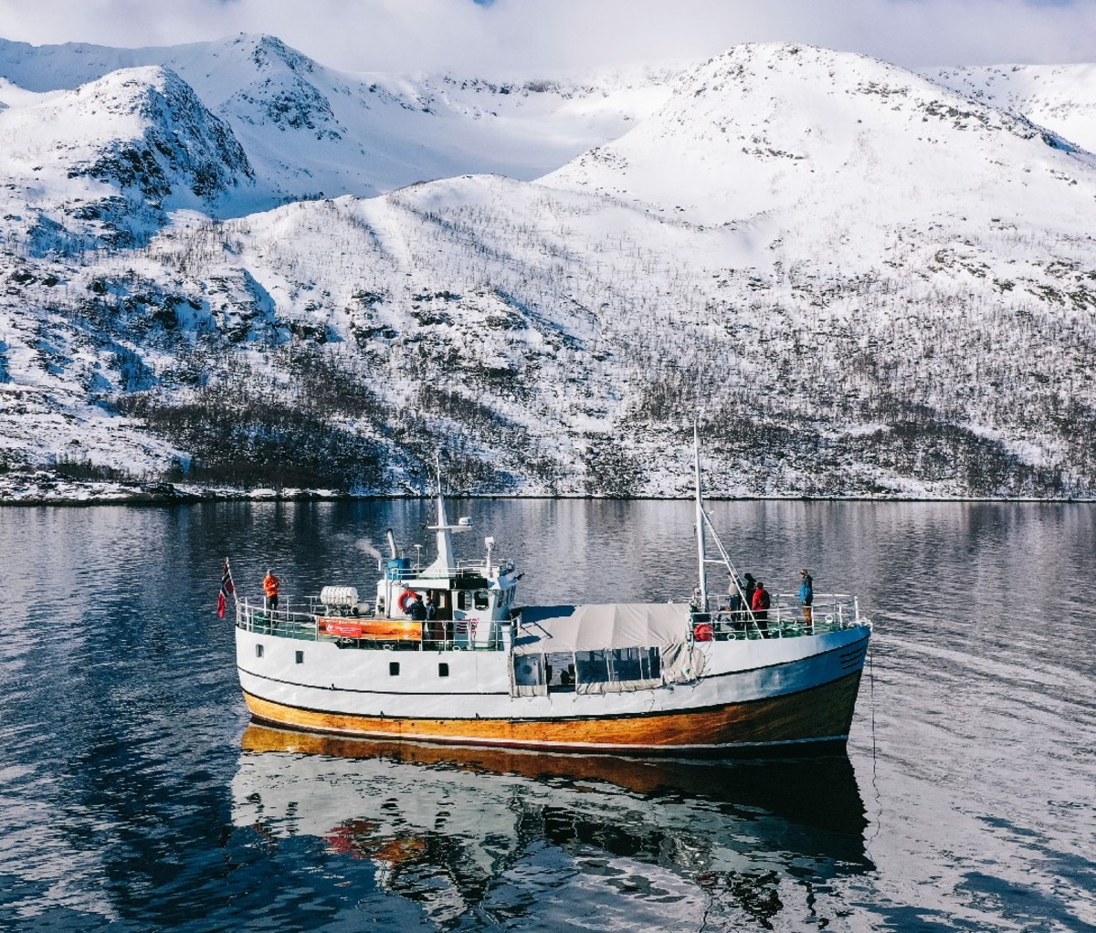 Ski trip charter boat anchored in a glassy lake in Northern Norway with snowy mountains in the background.