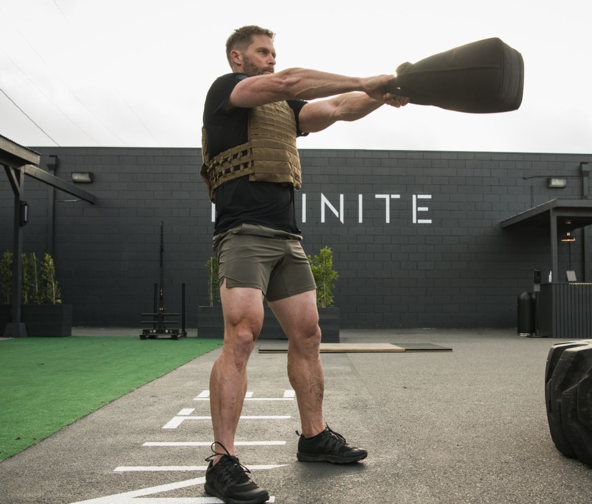 Athletic man swinging sandbag while wearing weight vest