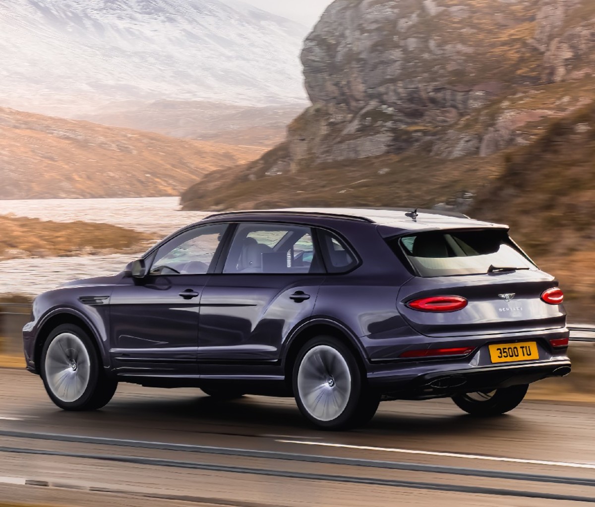 Rear-side profile of a dark colored 2023 Bentley Bentayga Extended Wheelbase driving on a mountain road