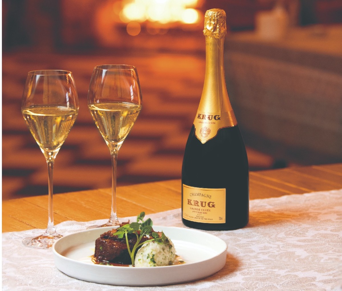 Table setting with a bottle of Krug champagne and two filled glasses beside a plate of braised beef short rib, Vermont wild rice and gremolata