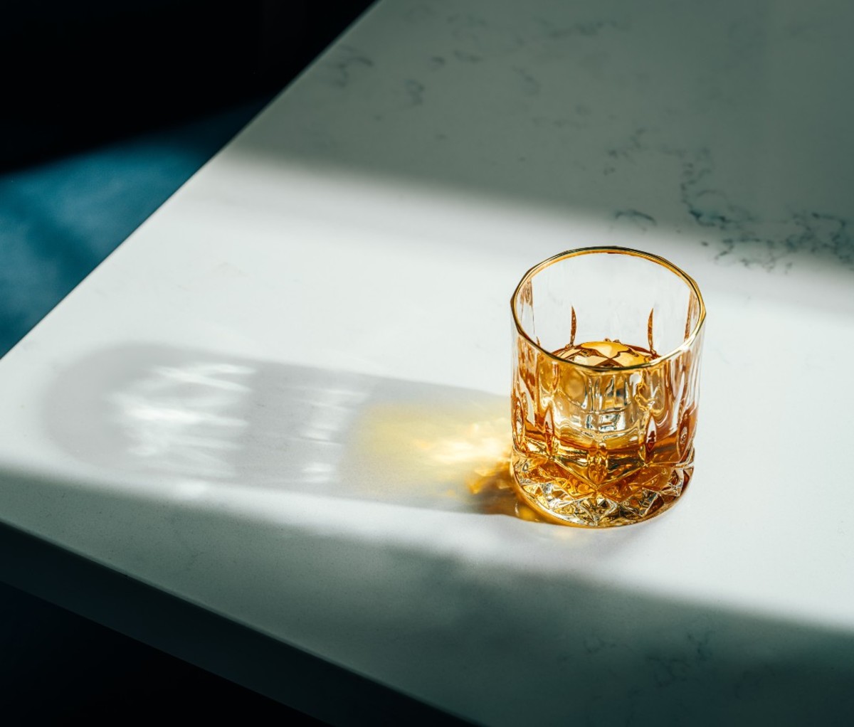 Glass of whiskey in sunlight on white tabletop