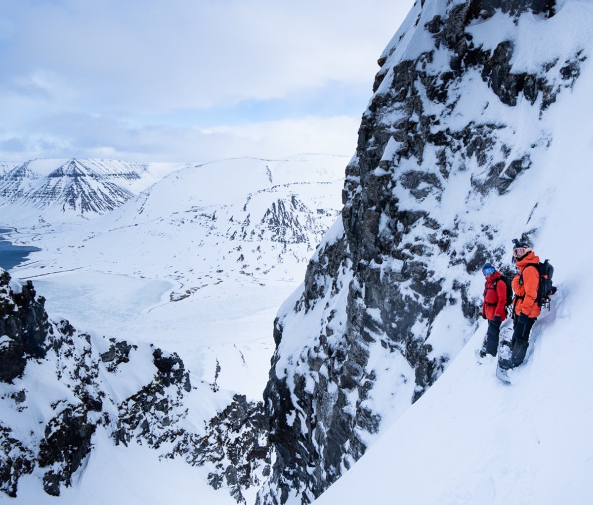 Two alpinists standing on side of mountain in red and orange jackets