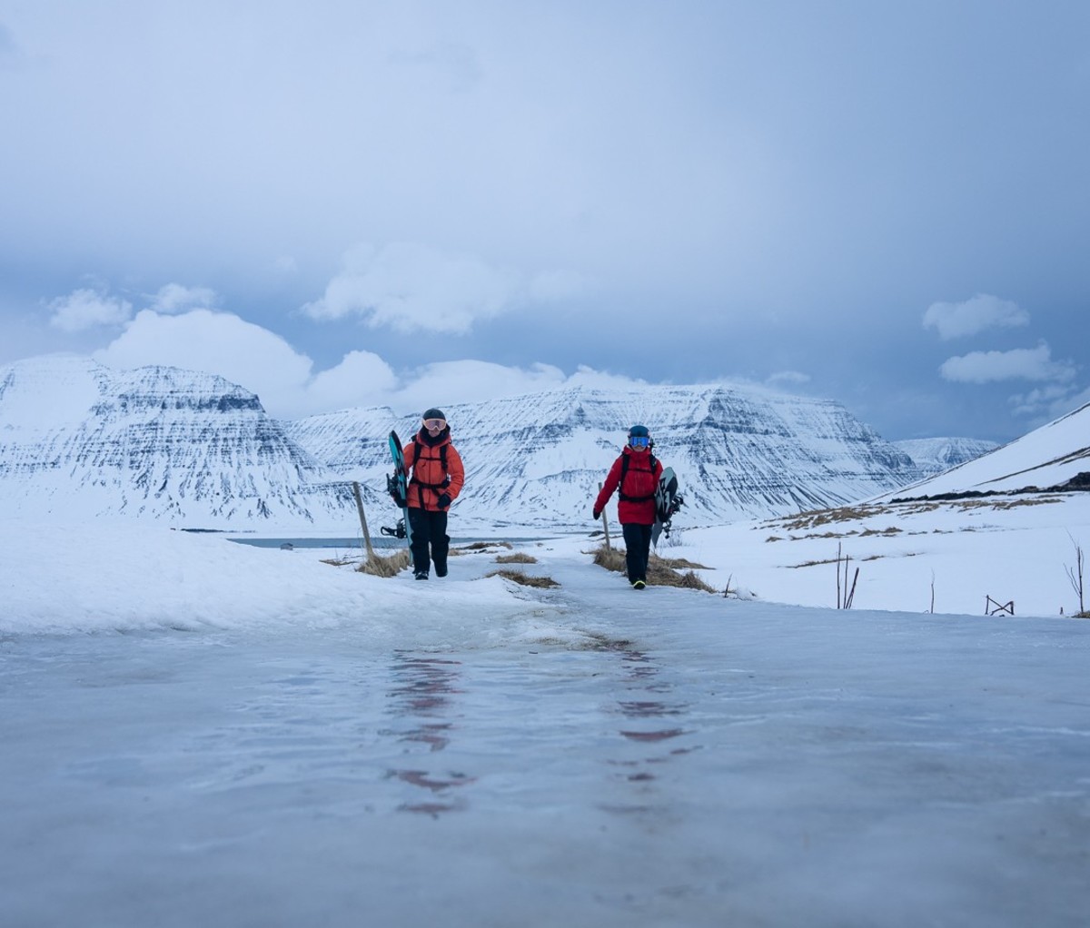 Two alpinists crossing water wearing red and orange jacket