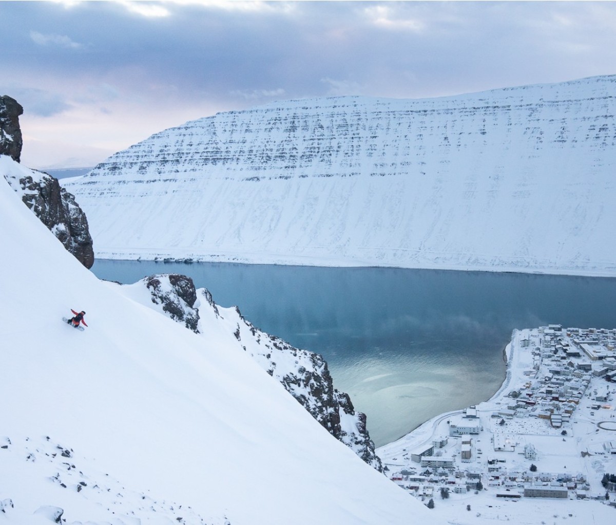 Aerial view of snowboarder going down mountain with village in background