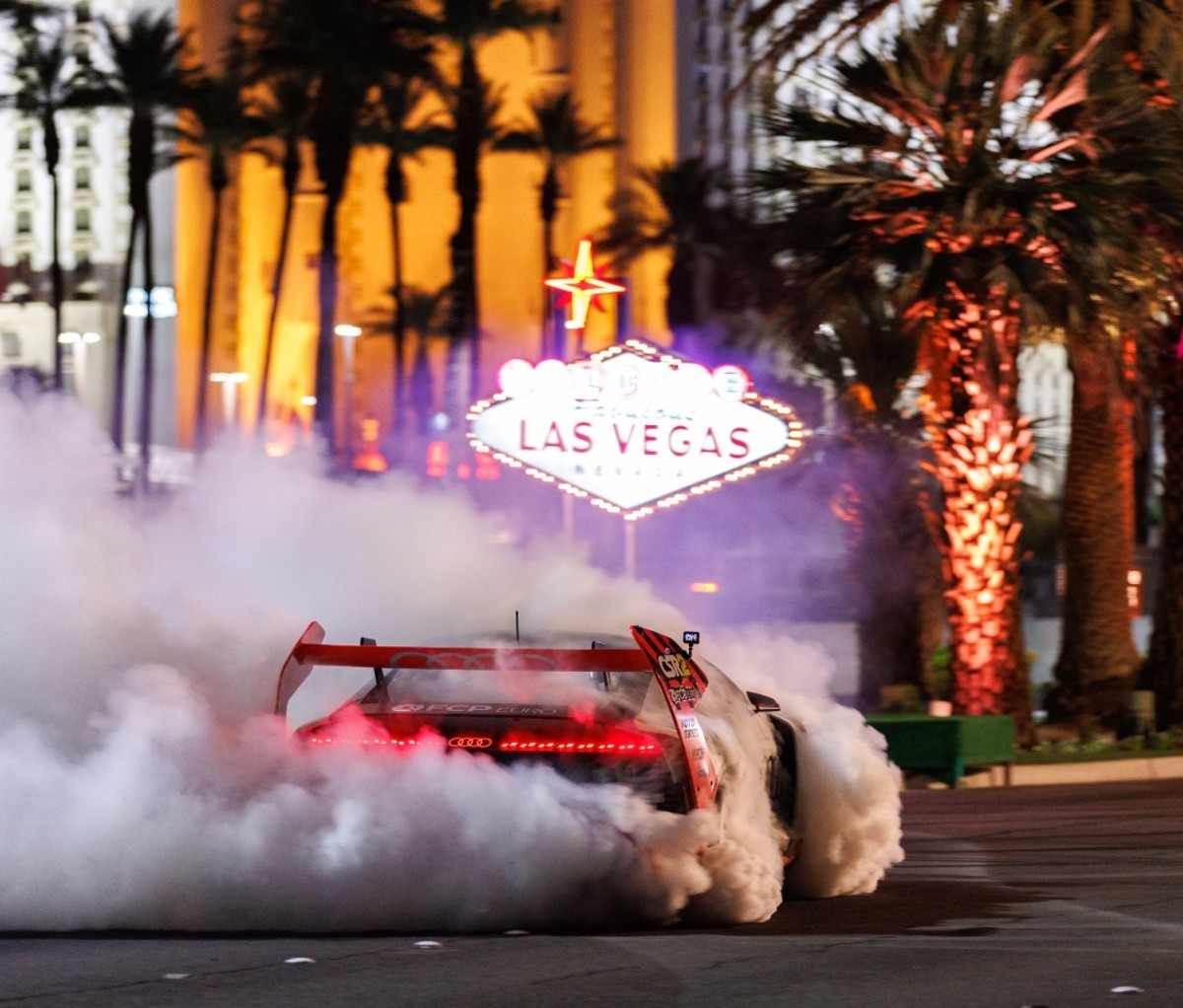 Ken Block's Audi Hoonitron EV racing car shreds tires in front of a Las Vegas sign.