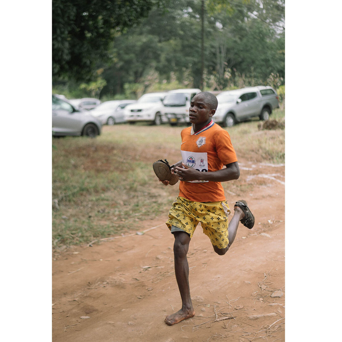 Young Malawian boy running in one sandal wearing orange shirt and yellow shorts