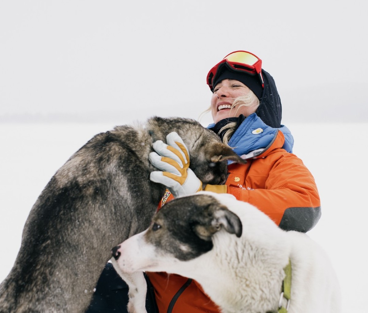 Woman in orange snowsuit holding sled dog in arms