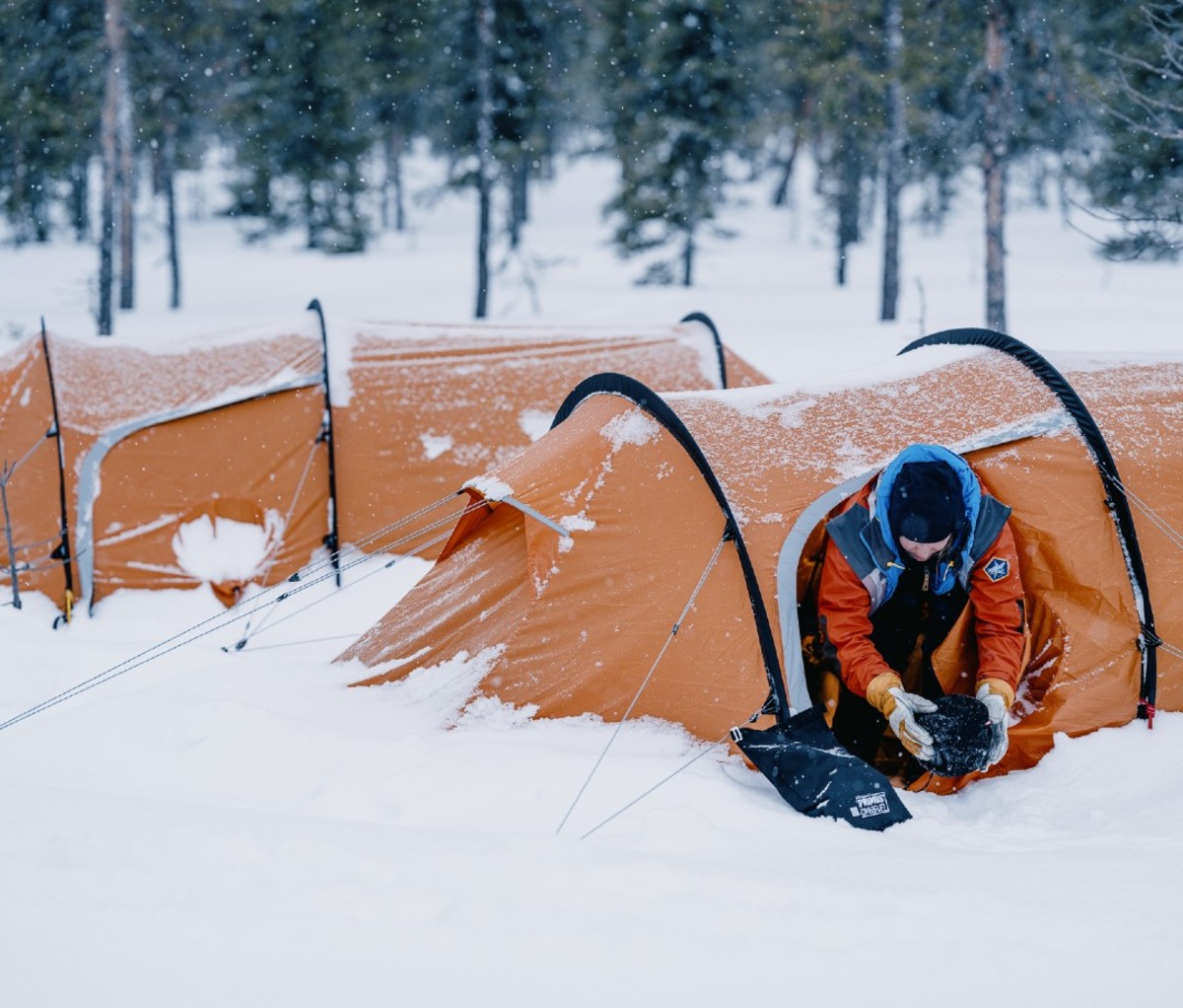 Woman holding gear as she crawls out of orange tent outdoors in snow