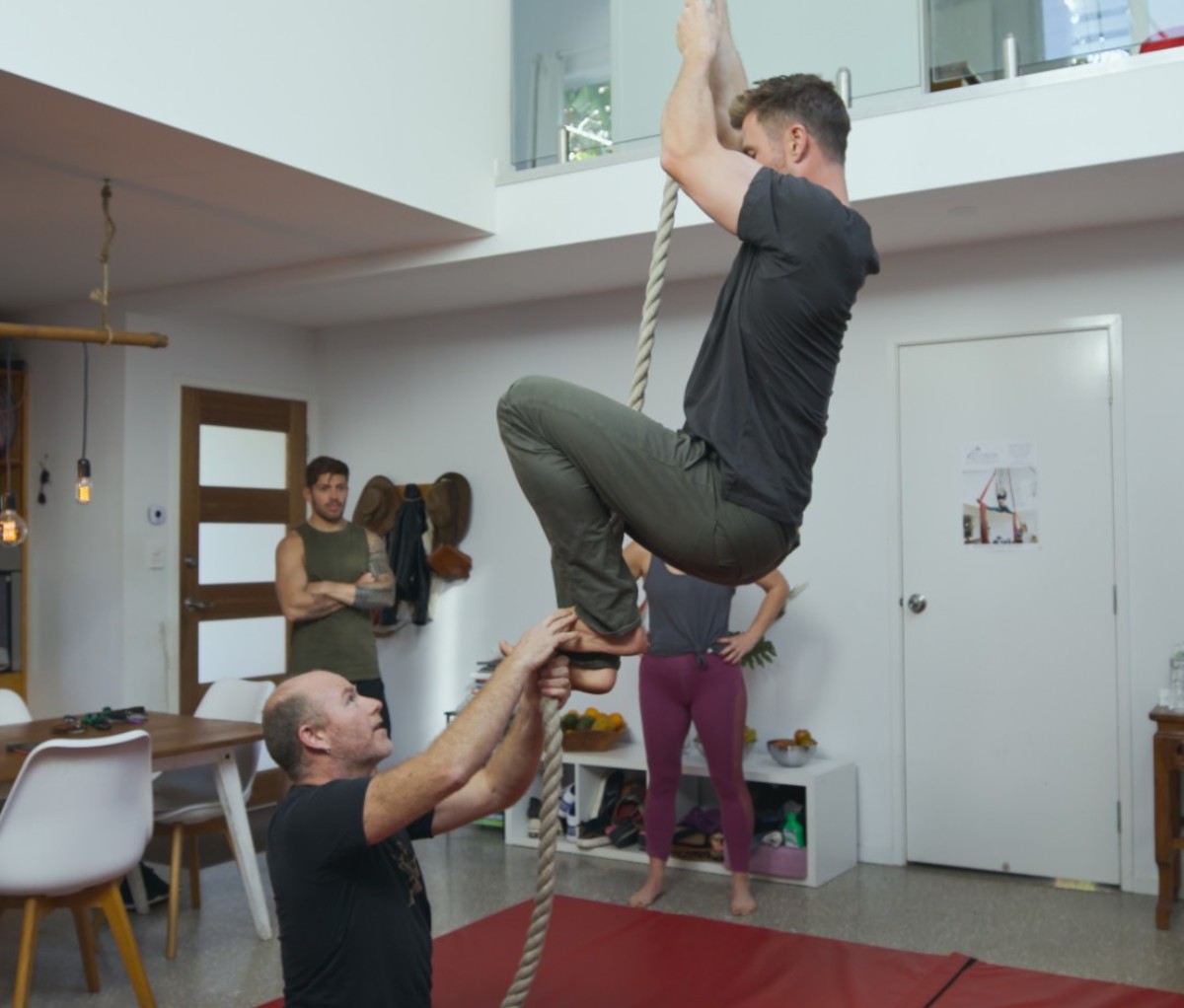 Caucasian man climbing rope with help of another man