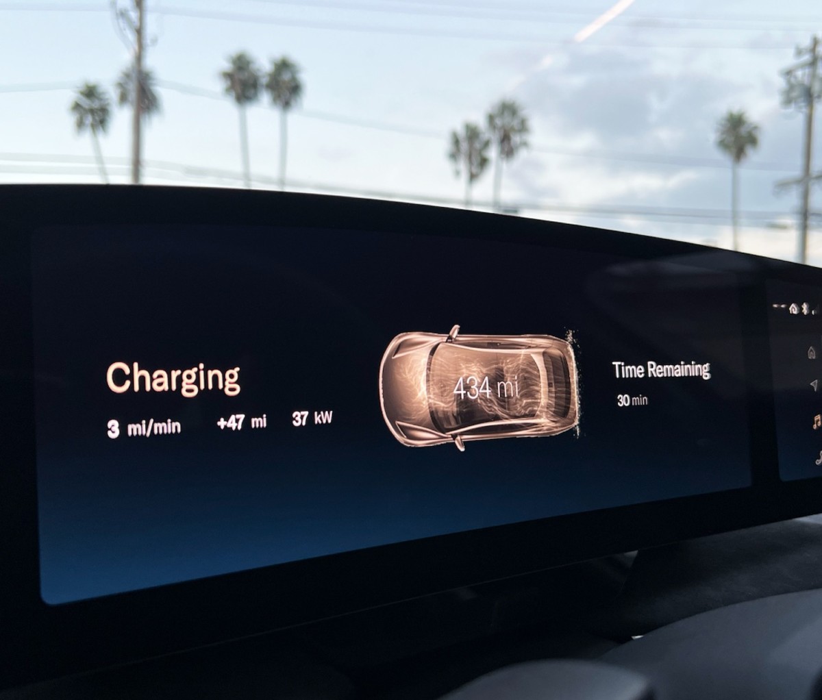 Lucid Air LCD panel showing charging status with palm trees in the background.