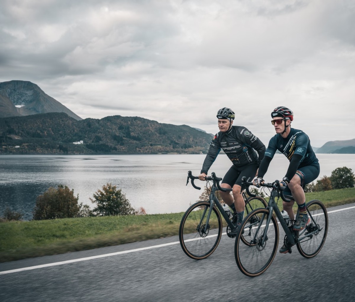 Two male cyclists riding on asphalt road by fjord