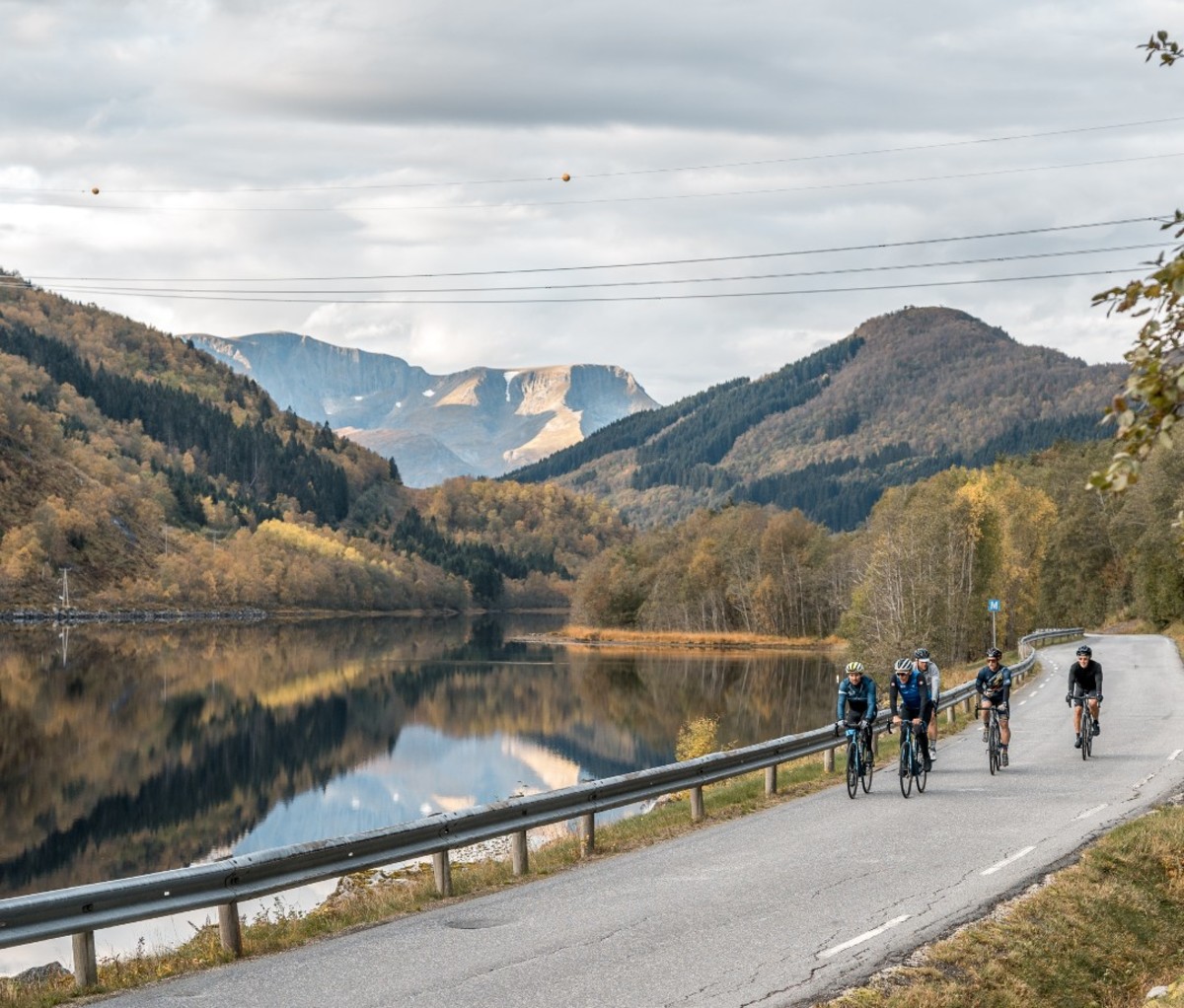 Group of cyclists riding on road by fjord and mountains