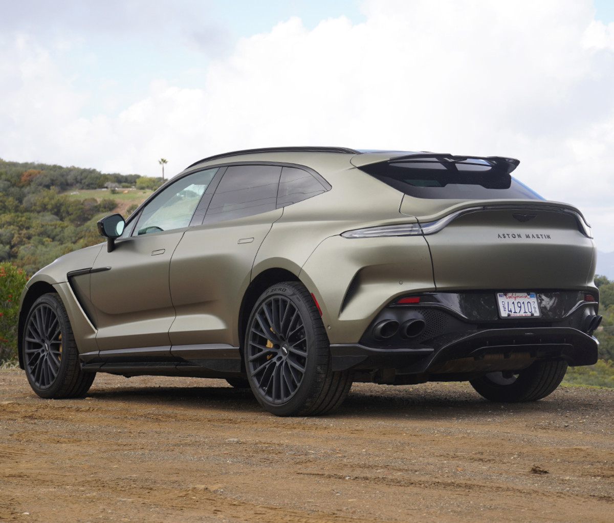 Bronze luxury SUV parked on dirt with trees in the background.