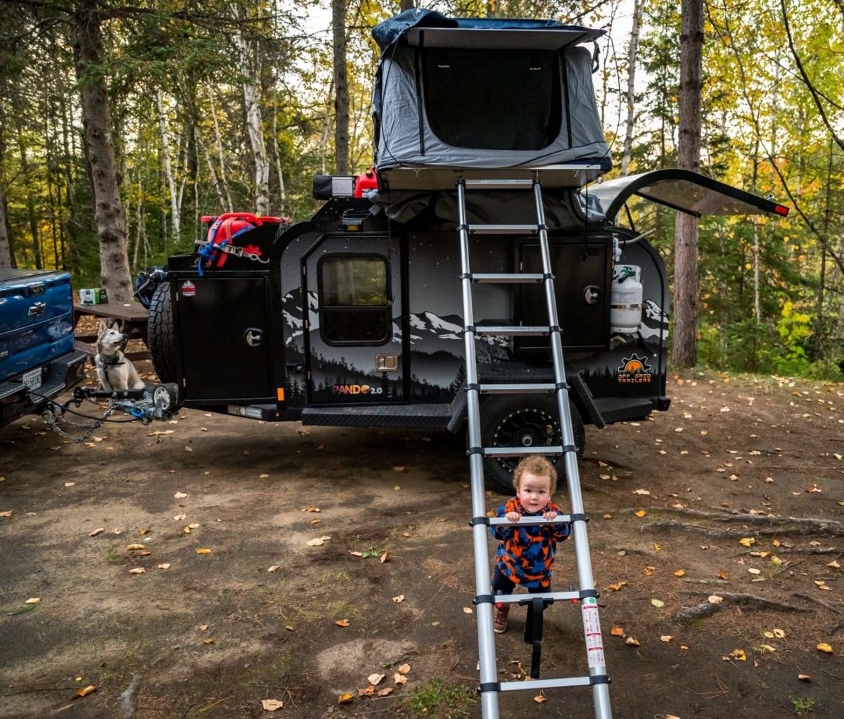 Young child next to a ladder to a rooftop tent on a camper trailer. Trans-Labrador Highway