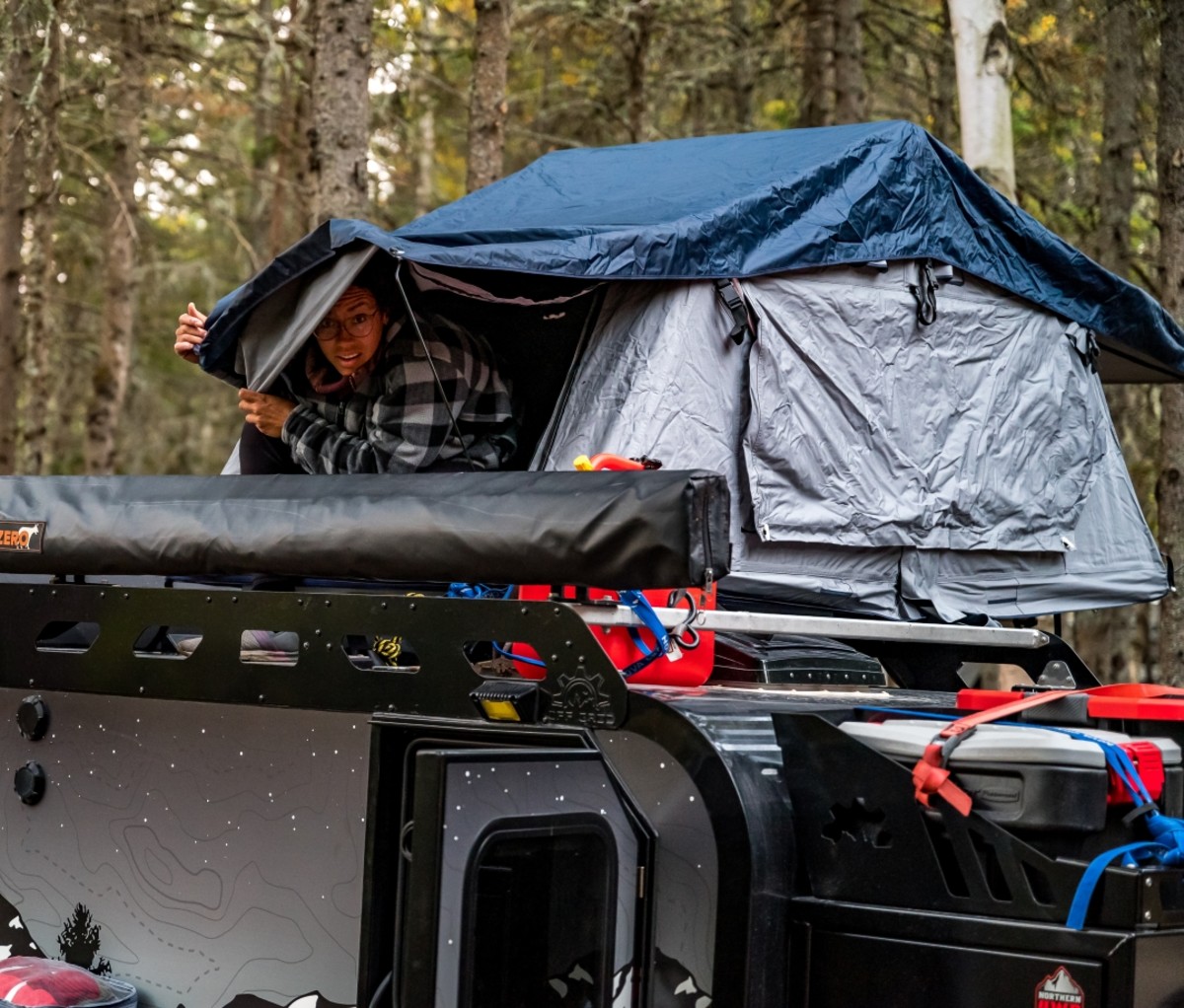 Woman inside a rooftop tent on a camper trailer looking out. Trans-Labrador Highway