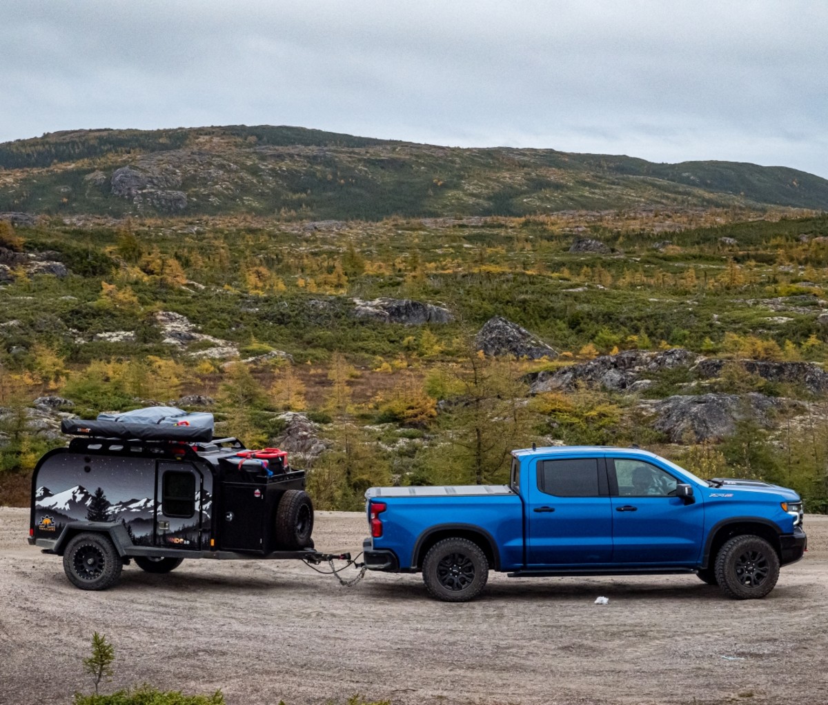 Blue pickup truck and teardrop camper trailer parked on a gravel road. Trans-Labrador Highway