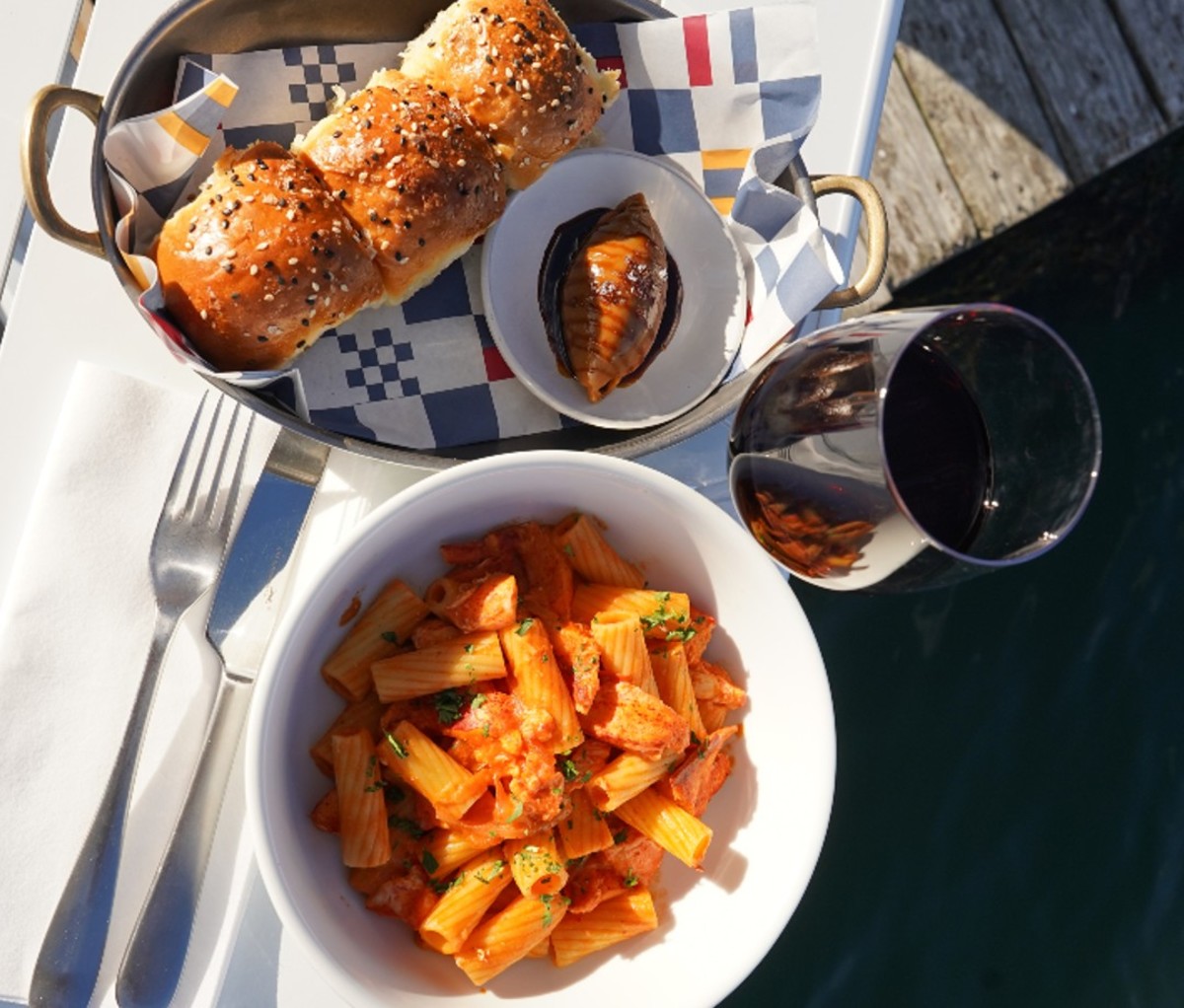 Plate of Lobster Rigatoni Alla Vodka with bread rolls and red wine