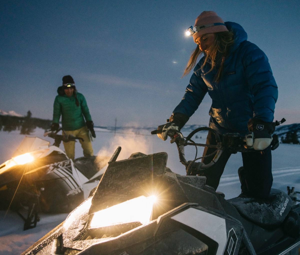 Snowmobilers on lit snowmobiles in the backcountry at night.