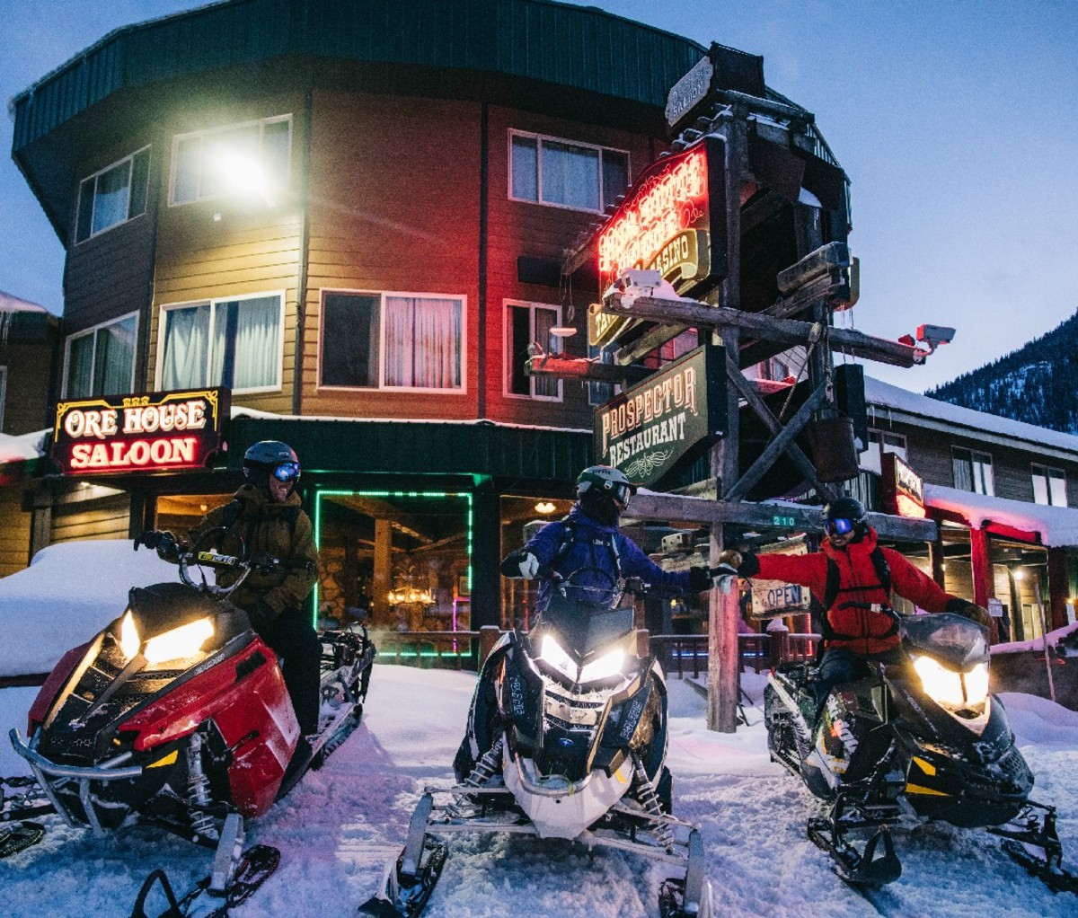 Three snowmobilers parked outside of a pub in Oregon.