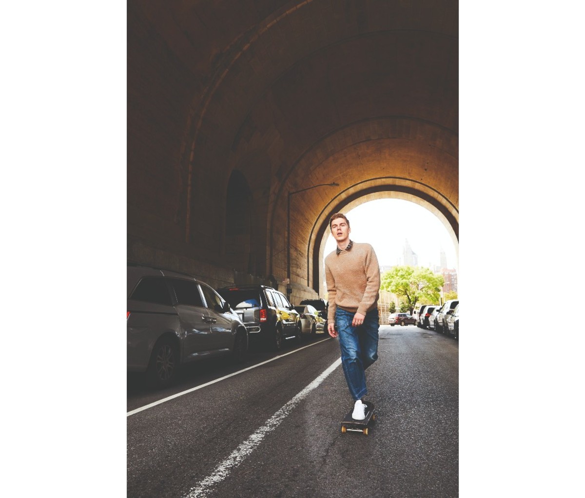 Man wearing a sweater and riding a skateboard through a tunnel.