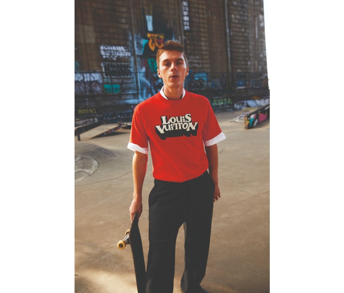 Man standing with a skateboard and wearing two shirts.