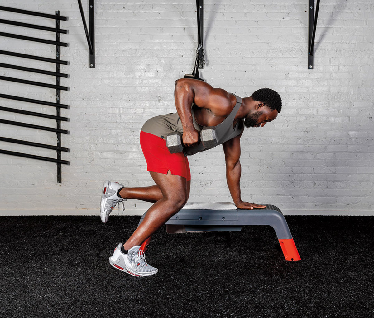 Black man wearing gray tank and red shorts doing Bench-supported Single-arm Row