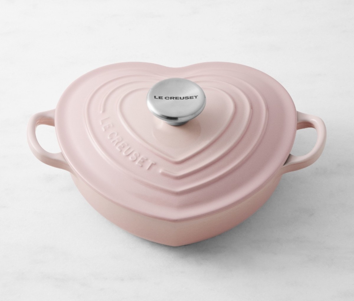 Pink, heart-shaped cast iron dutch oven on a marble counter.