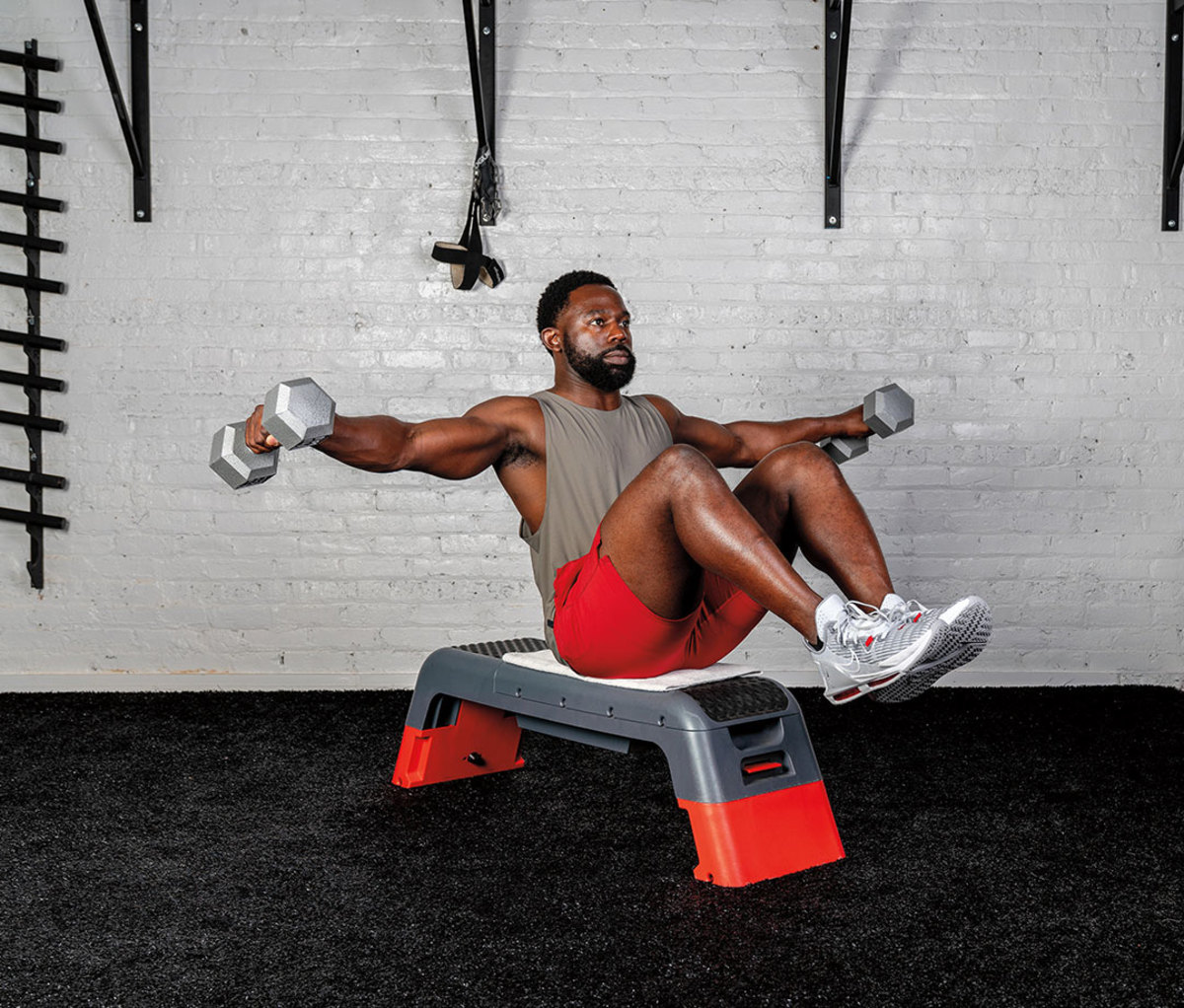 Black man wearing gray tank and red shorts doing Seated Balancing Lateral Raise