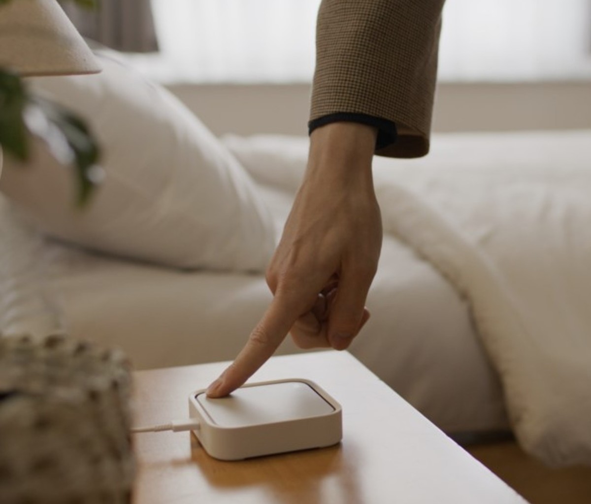 Finger touching smart hub device plugged into wall on bedside table