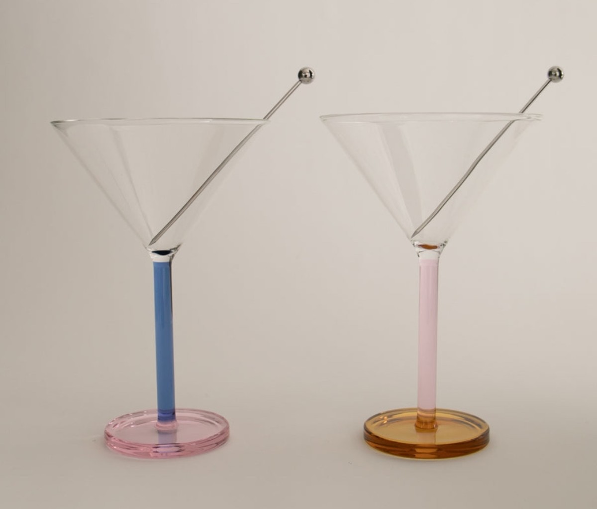 Two colorful martini-style cocktail glasses on an off-white background.