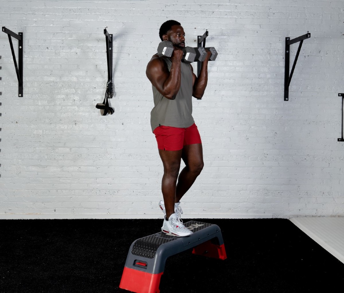 Black man wearing gray tank and red shorts doing Bench Step-up Biceps Curl