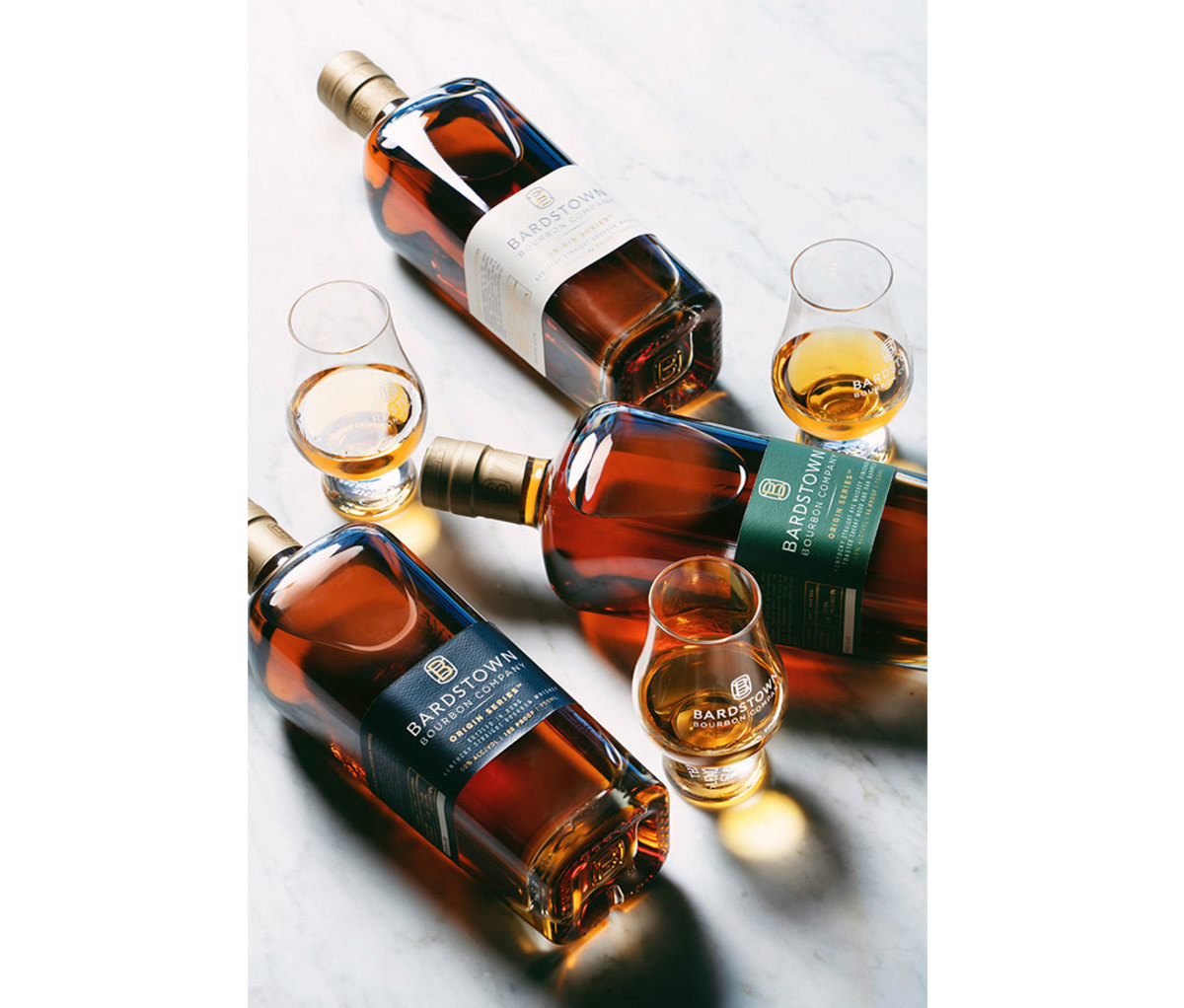 Three whiskeys lying on side on bar with navy, white, and green labels and accompanying glasses