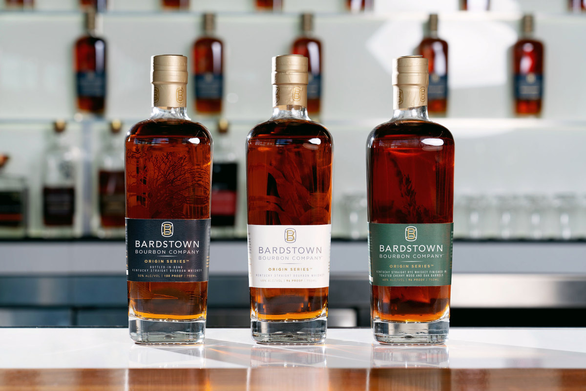 Lineup of three whiskeys on bar with navy, white, and green labels