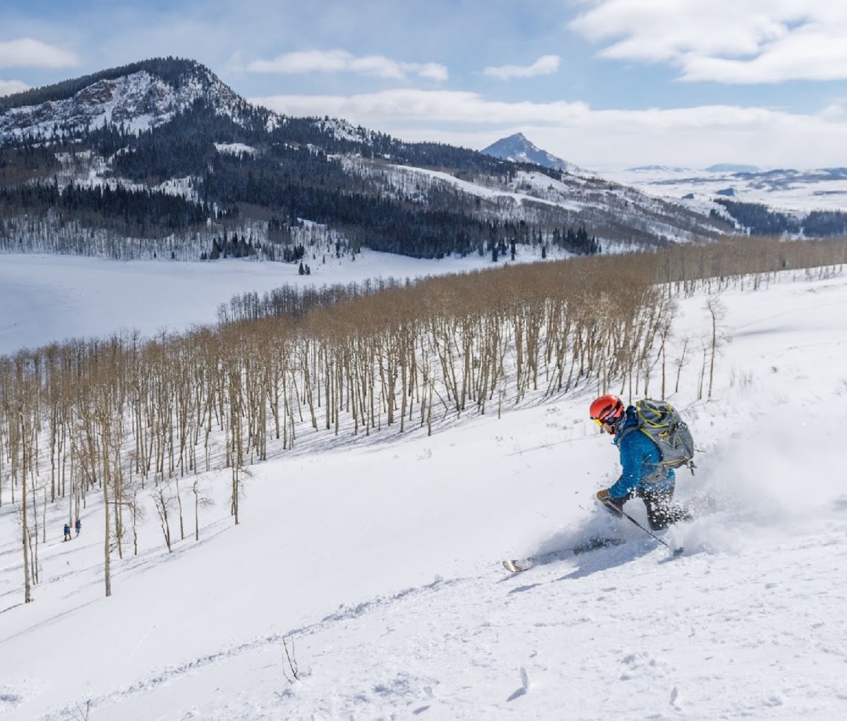 Man skiing in backcountry with brown grass and a large mountain in the background.