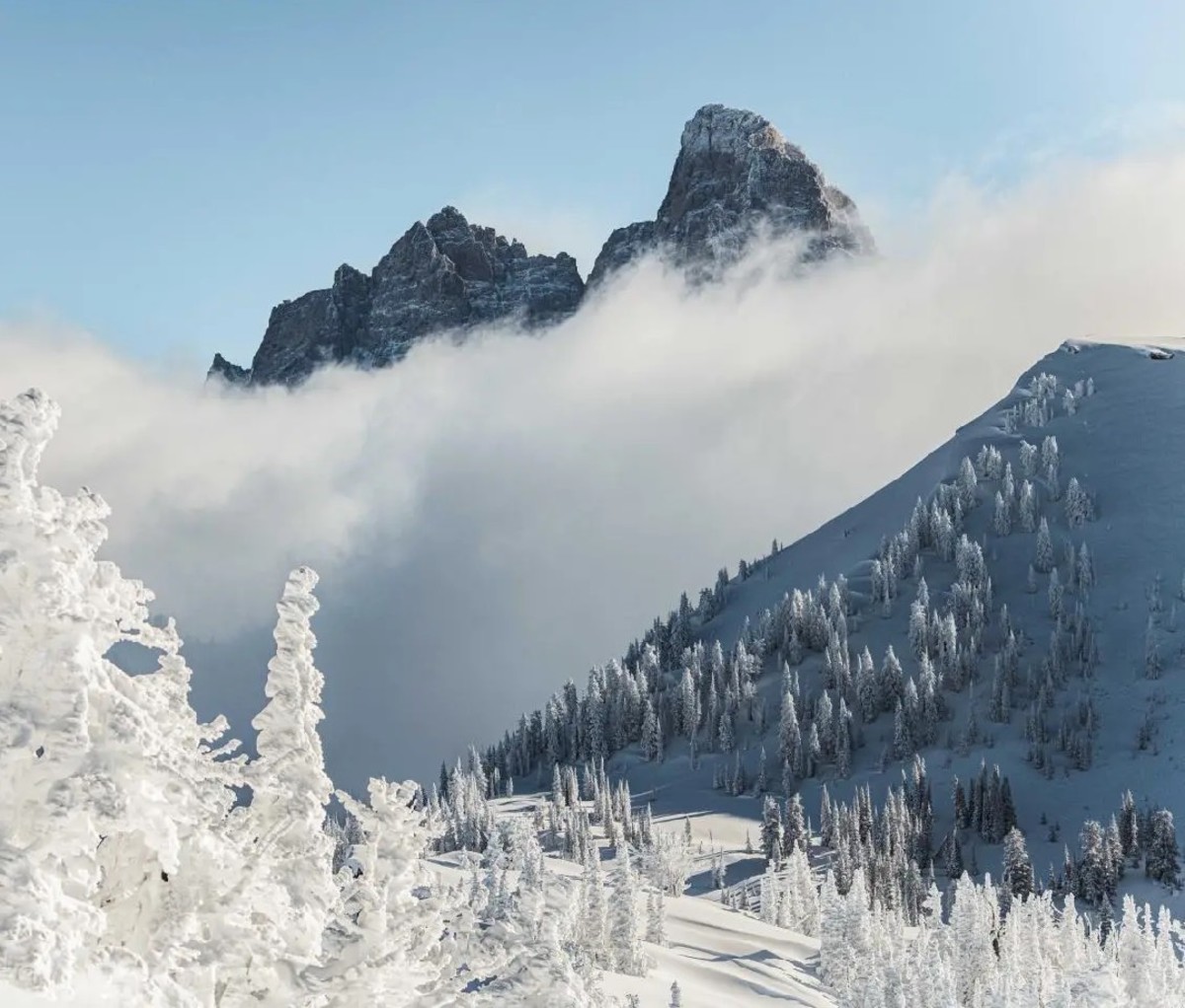 Snowy landscape with a small mountain and clouds in front of a massive mountain in the background.