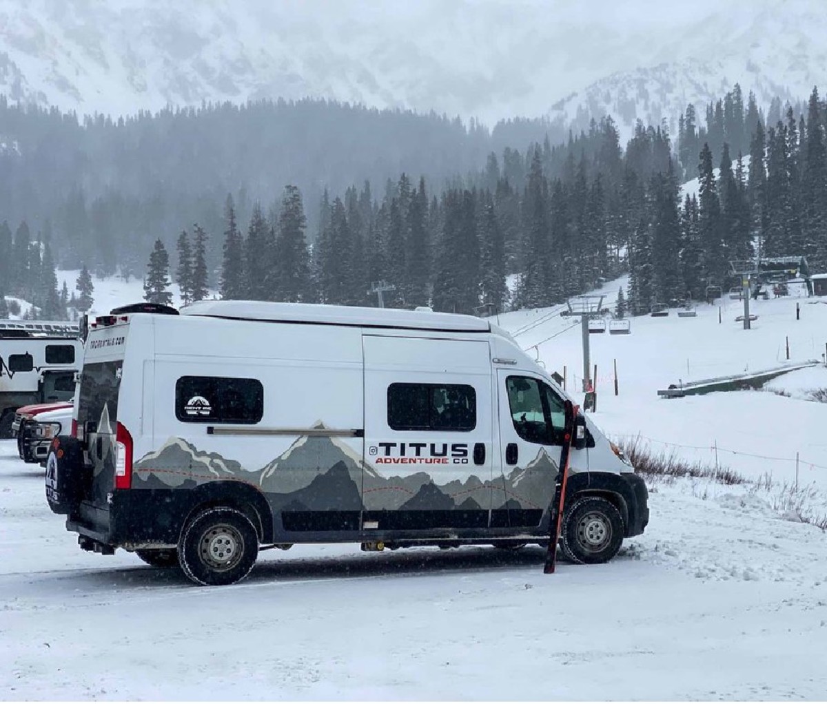 Camper van parked in a ski resort parking lot with chair lifts in the background.